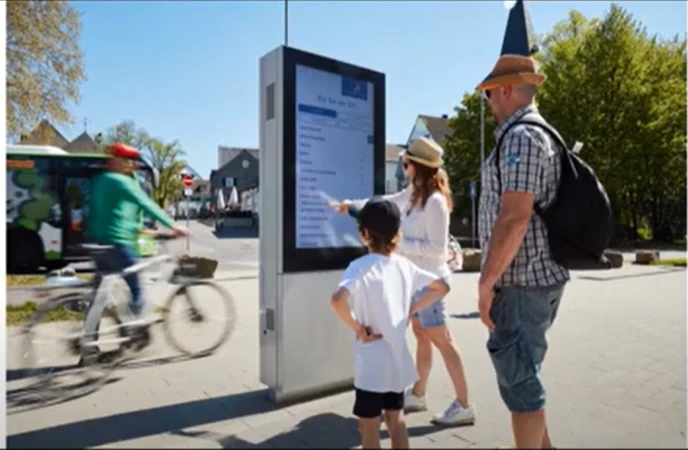 Drei Menschen vor digitale Anzeigetafel in Stadt